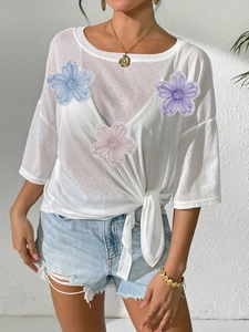 Detail of white loose top featuring 3D floral appliques and a stylish front knot design
