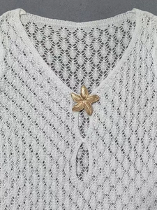 Détail de la robe de plage crochetée blanche avec fermoir étoile de mer doré sur le col V