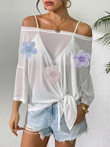 Close-up of white off-shoulder mesh top featuring colorful floral embroidery and tie-knot hem