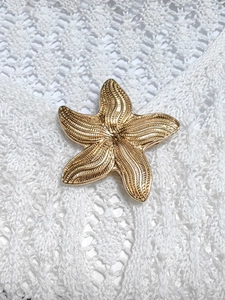 Vue détaillée d'une broche étoile de mer dorée sur un fond en dentelle crochetée blanche