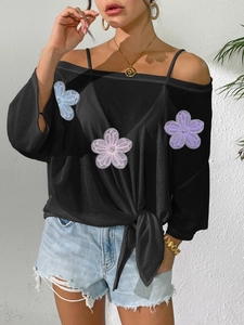 Detail of off-shoulder black blouse with floral appliques and front tie knot waist