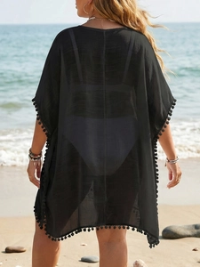 Détail de la tunique de plage noire avec bordure à pompons et tissu en maille transparente