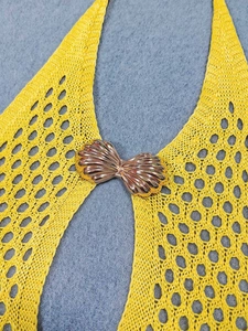 Detail of yellow crochet knit dress featuring a gold shell buckle and hollow mesh texture