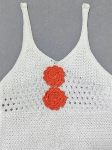 Close-up of white crochet beach dress featuring orange floral hand-knitted embroidery