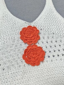 Detail of white crochet summer top with handmade orange floral accents and knit texture