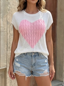 Detail of white knit top featuring a pink cable-knit heart pattern and crew neckline
