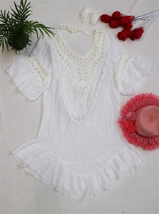 Detail of white crochet knit beach cover-up featuring lace neckline and ruffled hemline