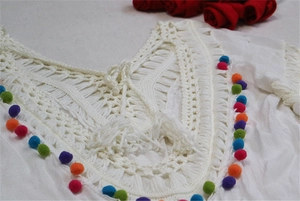 Detailed view of white knit beach cover-up featuring colorful pom poms and V-neckline