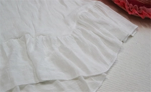 Detail of white knit beach cover-up featuring ruffled hem and textured fabric finish