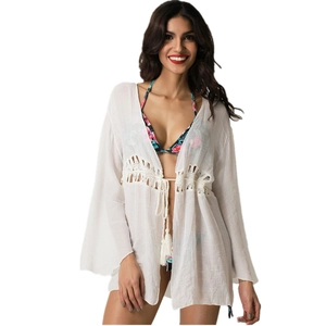 Detail of white crochet beach cover-up featuring bell sleeves and tassel drawstring waist