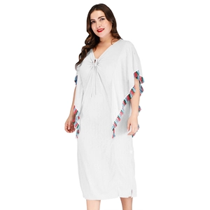 Détail d'un caftan blanc bohème avec pompons colorés aux manches et à l'ourlet