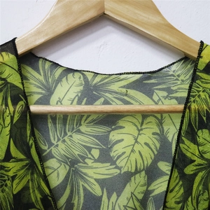 Close-up of tropical green leaf print with fine black overlock stitching on thin fabric