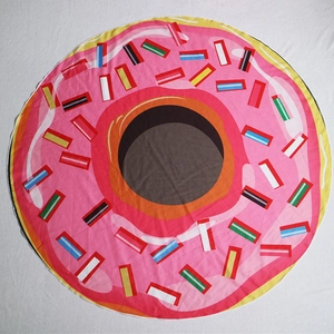 Overhead view of a round pink donut printed beach towel with colorful sprinkles pattern