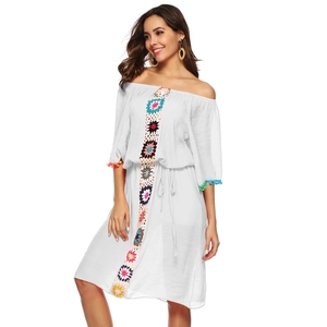 Détail d'une robe de plage blanche à épaules dénudées avec crochet floral et pompons