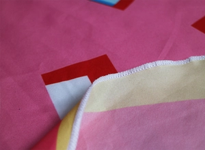 Macro shot of pink fabric showing fine white overlock stitching on geometric printed towel