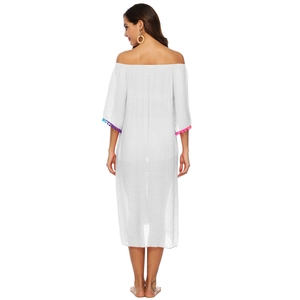 Détail d'une robe de plage blanche à épaules dénudées avec pompons colorés aux manches