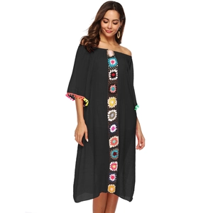 Détail de la broderie florale au crochet et des glands pompons sur une robe de plage noire