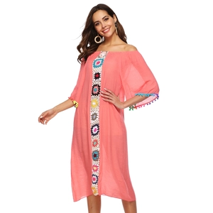 Détail des fleurs au crochet et des franges à pompons sur la robe de plage rose boho