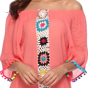 Détail d'un haut corail à épaules dénudées avec fleurs au crochet et franges à pompons