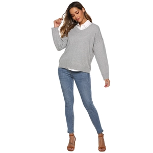 Detailed full-body shot of a grey V-neck knit sweater layered with a white shirt and denim jeans