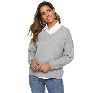 Detail of grey V-neck knitted sweater layered with white shirt and light blue denim jeans