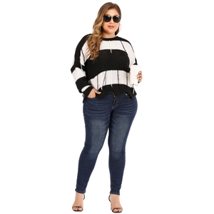Detail of plus size striped knit sweater with tassel fringe hem and blue skinny jeans