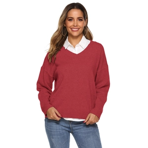 Detail of red V-neck knitted sweater layered with white shirt and blue jeans