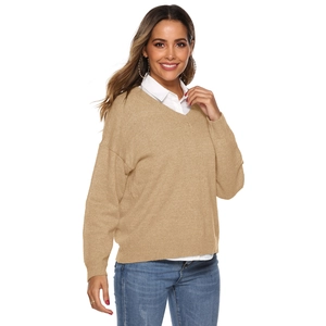 Detail view of khaki V-neck knitted sweater layered with a white shirt and denim jeans