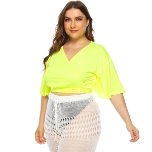 Detail of neon yellow V-neck wrap top with textured fabric and white crochet knit trousers