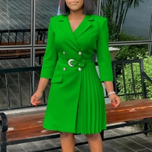 Detail of bright green double-breasted suit dress with metal buckle belt and pleated hem