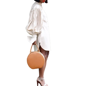 Detail of puffed long sleeves on an ivory shirt dress paired with a round brown leather bag