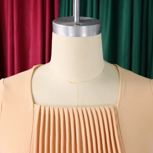 Macro shot of fine accordion pleats and square neckline on a beige chiffon dress