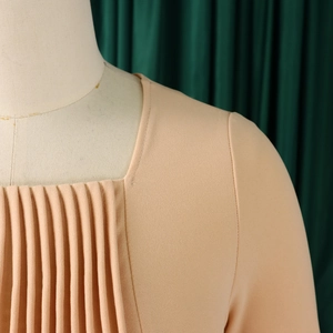 Detailed close-up of square neck dress with pleated bodice design in apricot fabric