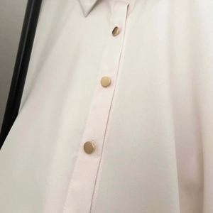 Close-up of golden metal buttons on cream-colored long sleeve puff sleeve shirt dress