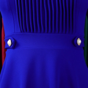 Close-up of royal blue dress with pleats and gold faux pearl buttons on the waist