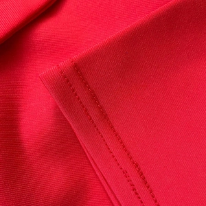 Close-up of red knit dress fabric showing fine mesh texture and double-stitch seam detail