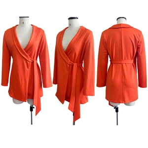 Detail of a bright orange wrap blazer dress featuring a deep V-neck and a waist tie belt
