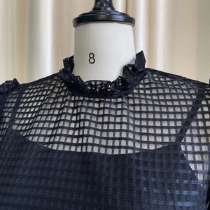 Detail of black grid lace top with a ruffled high neck and sheer puff sleeve texture