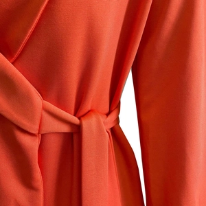 Close-up of bright orange dress featuring V-neckline and tie-waist detail with knit texture