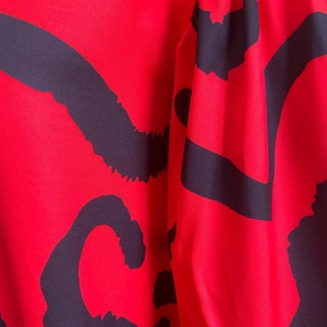 Close-up of red fabric featuring abstract black brushstroke patterns on casual shirt dress