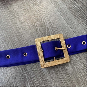 Dettaglio della cintura in tessuto blu reale con una grande fibbia quadrata in metallo dorato