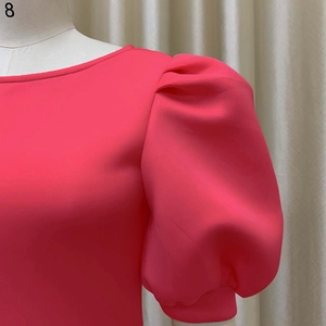 Détail des manches bouffantes et de l'encolure ronde sur une robe de soirée rose fuchsia