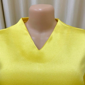 Dettaglio dell'elegante scollo a V su camicetta di raso giallo con tessuto lucido