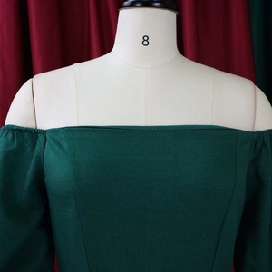 Detail of dark green off-shoulder dress featuring textured fabric and bell sleeves on a model