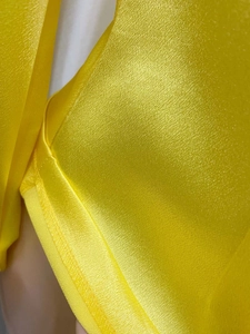 Macro del tessuto di raso giallo brillante che mostra dettagli di trama e cuciture del top