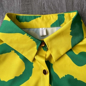 Detail of the shirt collar with yellow and green abstract print and a gold button