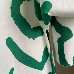 Close-up detail of smooth white satin fabric with green abstract art floral prints