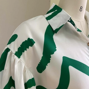 Detail of white shirt dress with green abstract print, lapel collar, and pleated puff sleeves