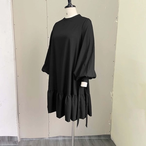 Detail of minimalist black loose dress featuring puff sleeves and a ruffled hemline