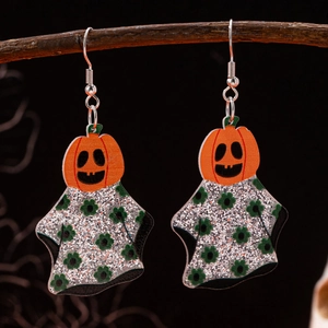 Detailed close-up of ghost pumpkin earrings with green floral patterns on dark wood